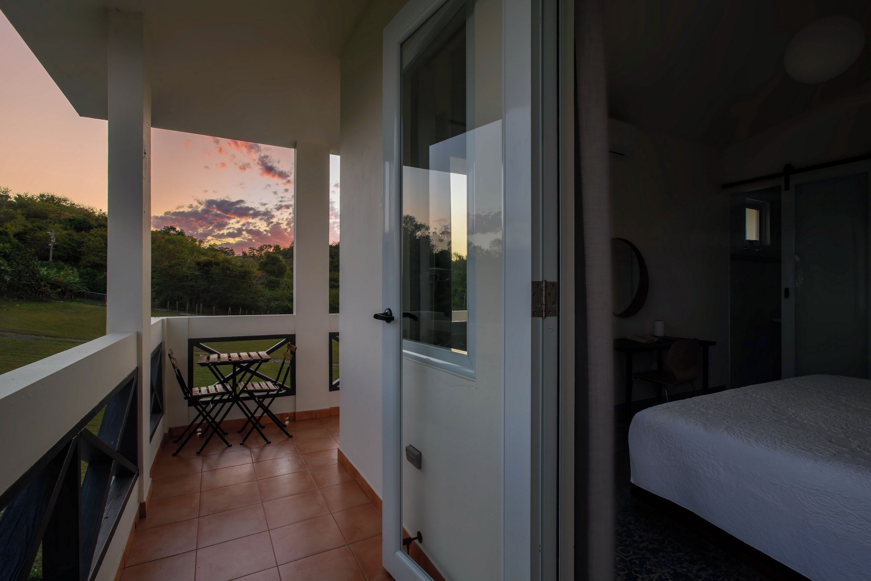 A balcony with a table and chairs, a bed, and a door leading to a room.