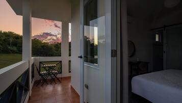 A balcony with a table and chairs, a bed, and a door leading to a room.