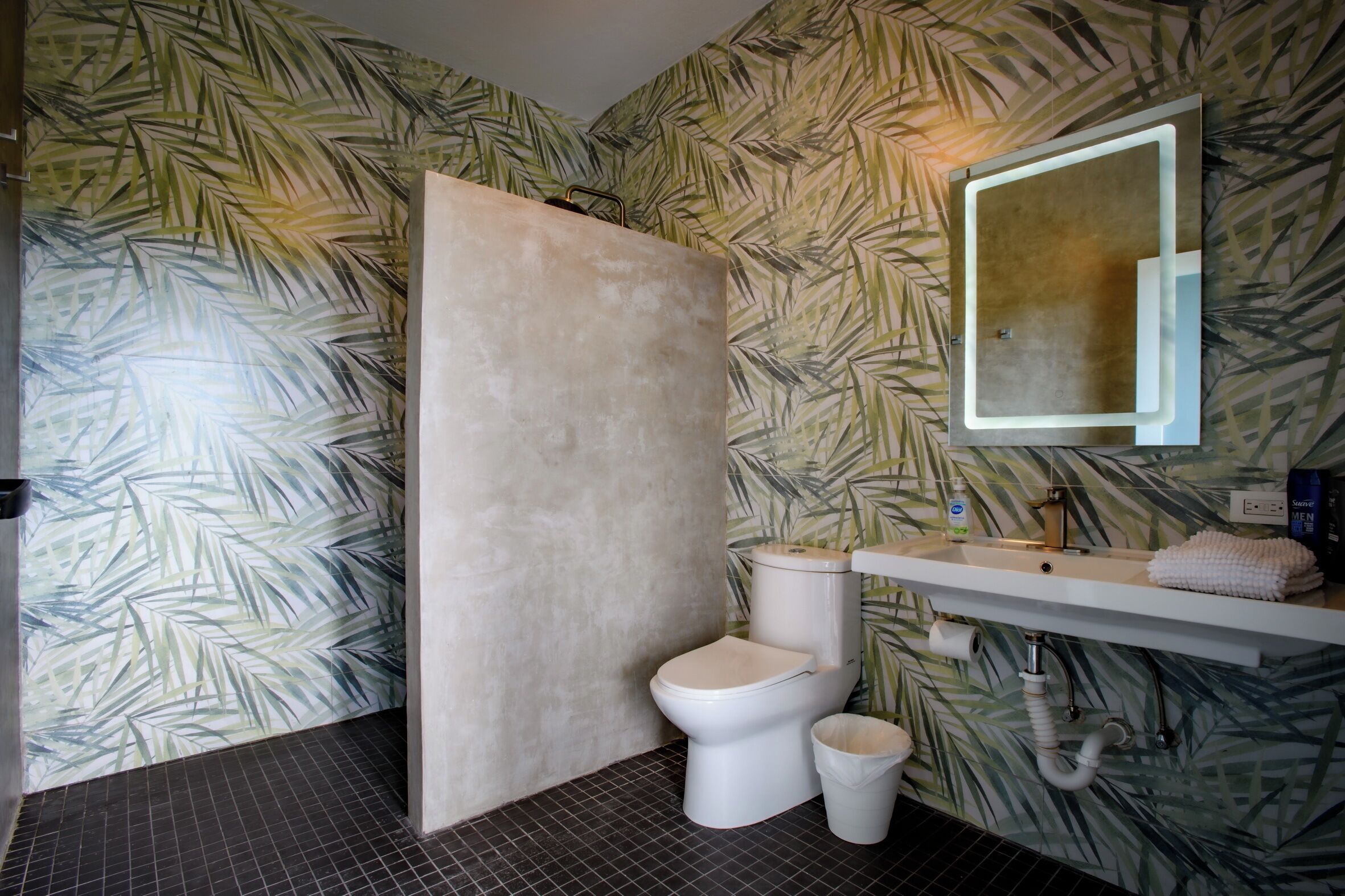 Een badkamer met toilet, wastafel en spiegel. De wanden zijn voorzien van behang met bladmotieven.
