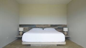 Un dormitorio con una cama centrada sobre una plataforma, flanqueada por dos mesitas de noche con lámparas, frente a una pared con diseño de paneles de madera.