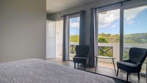 A bedroom with a large bed, two chairs, a small table, and a balcony with a view of greenery. - Club Vieques - Adults Only Resort - LGBT Friendly (Vieques)