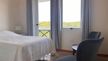 A hotel room with a bed, a chair, a small table, and a view of a balcony with curtains.