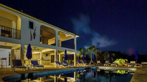Ein zweistöckiges Hotel mit Swimmingpool, Liegestühlen und Sonnenschirmen.