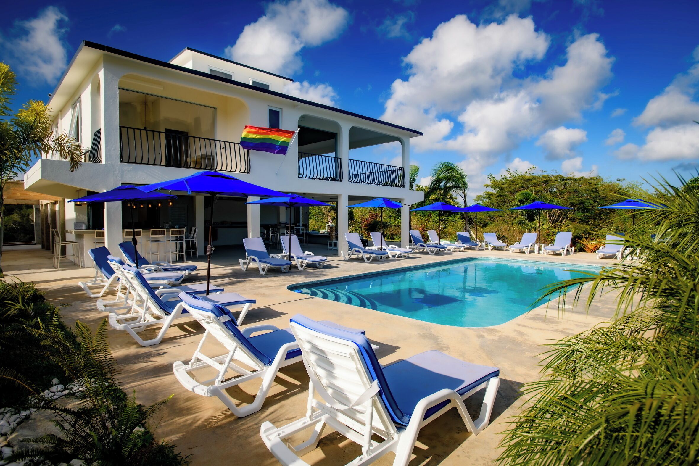 A poolside area with lounge chairs and umbrellas, a clear blue sky, and a building with a balcony.
