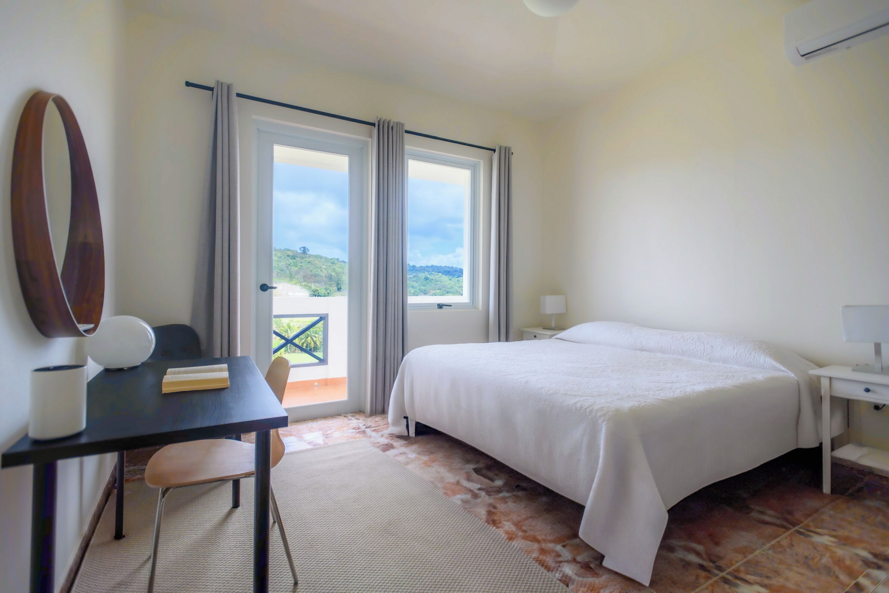 Une chambre d’hôtel équipée d’un lit, d’un bureau, d’une chaise, d’une lampe et offrant une vue sur l’extérieur.