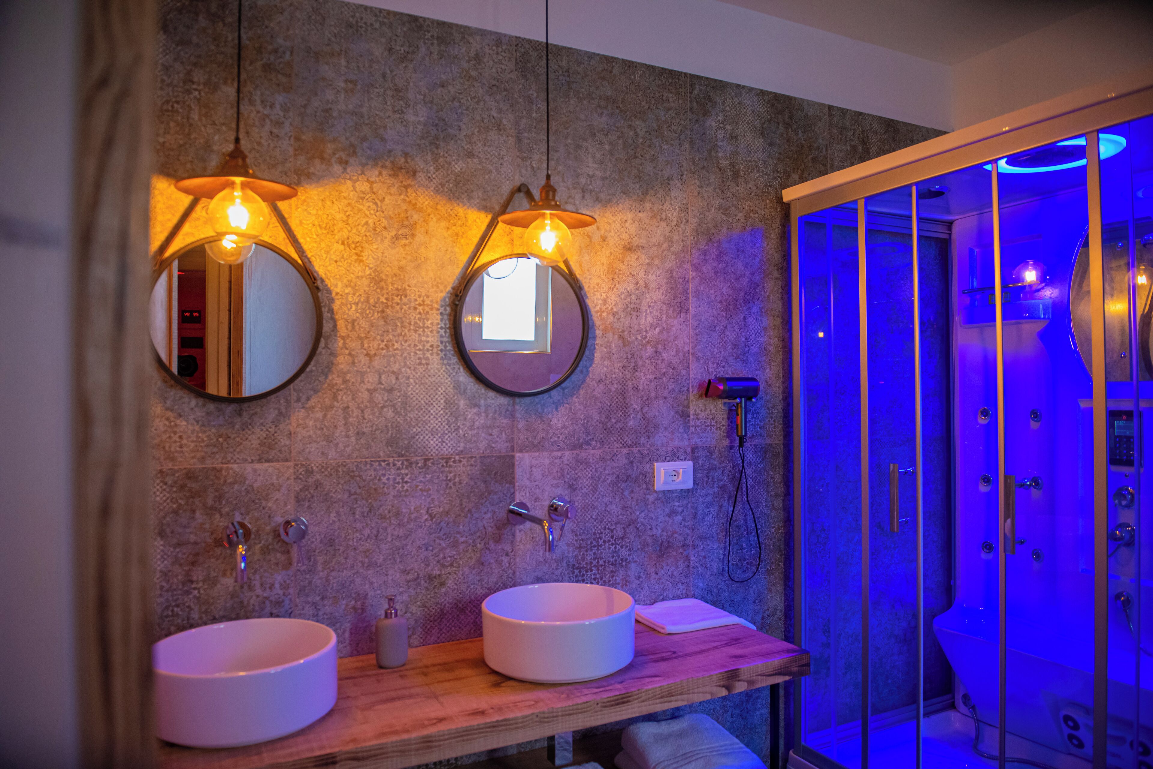 Un bagno con due specchi circolari, un mobile bagno in legno e un box doccia in vetro.