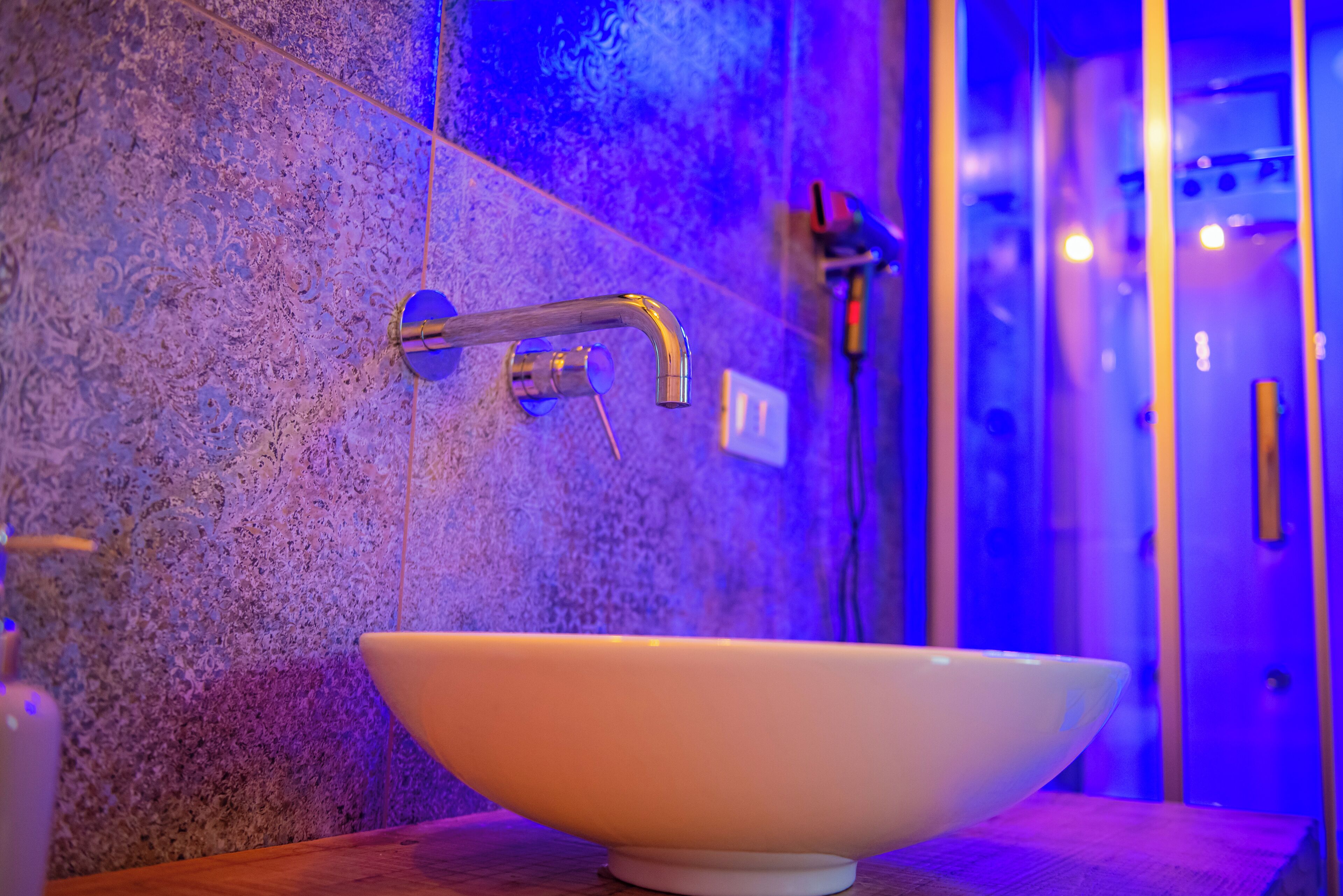 Ein Badezimmer mit einem weißen Waschbecken, einem modernen Wasserhahn und einer strukturierten Wand.