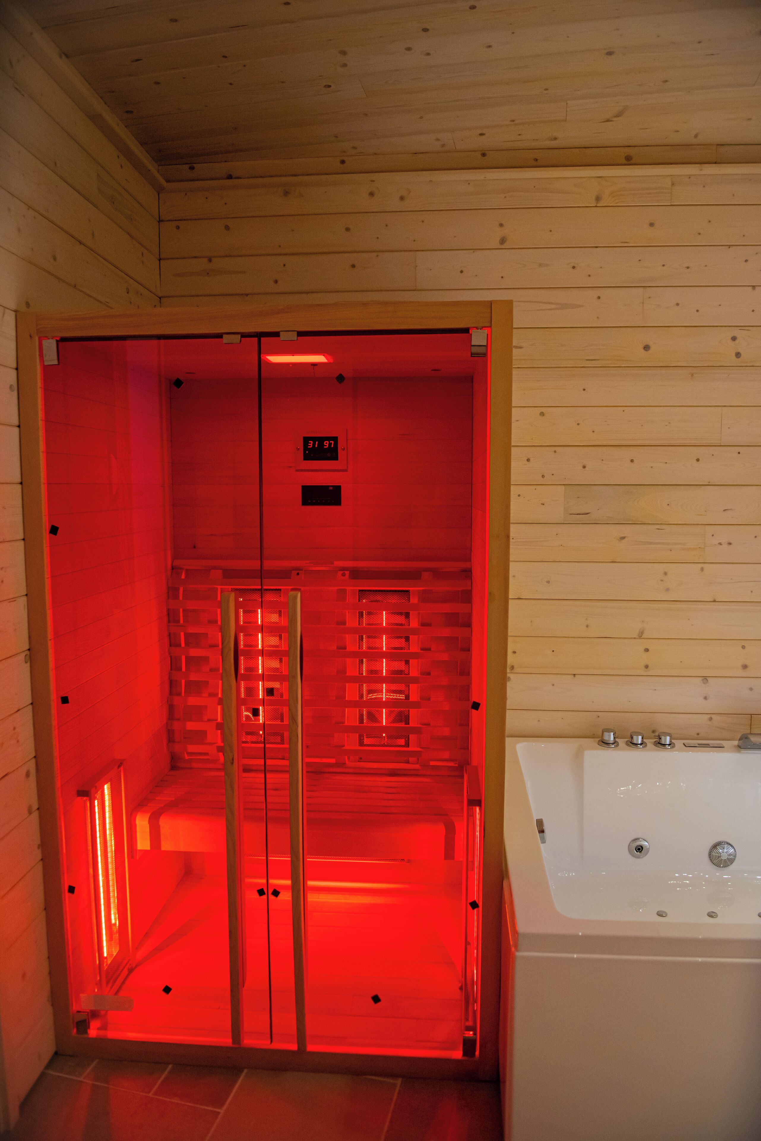 Een sauna met houten inrichting, een glazen deur en een wit bad.