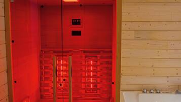 Een sauna met houten inrichting, een glazen deur en een wit bad.