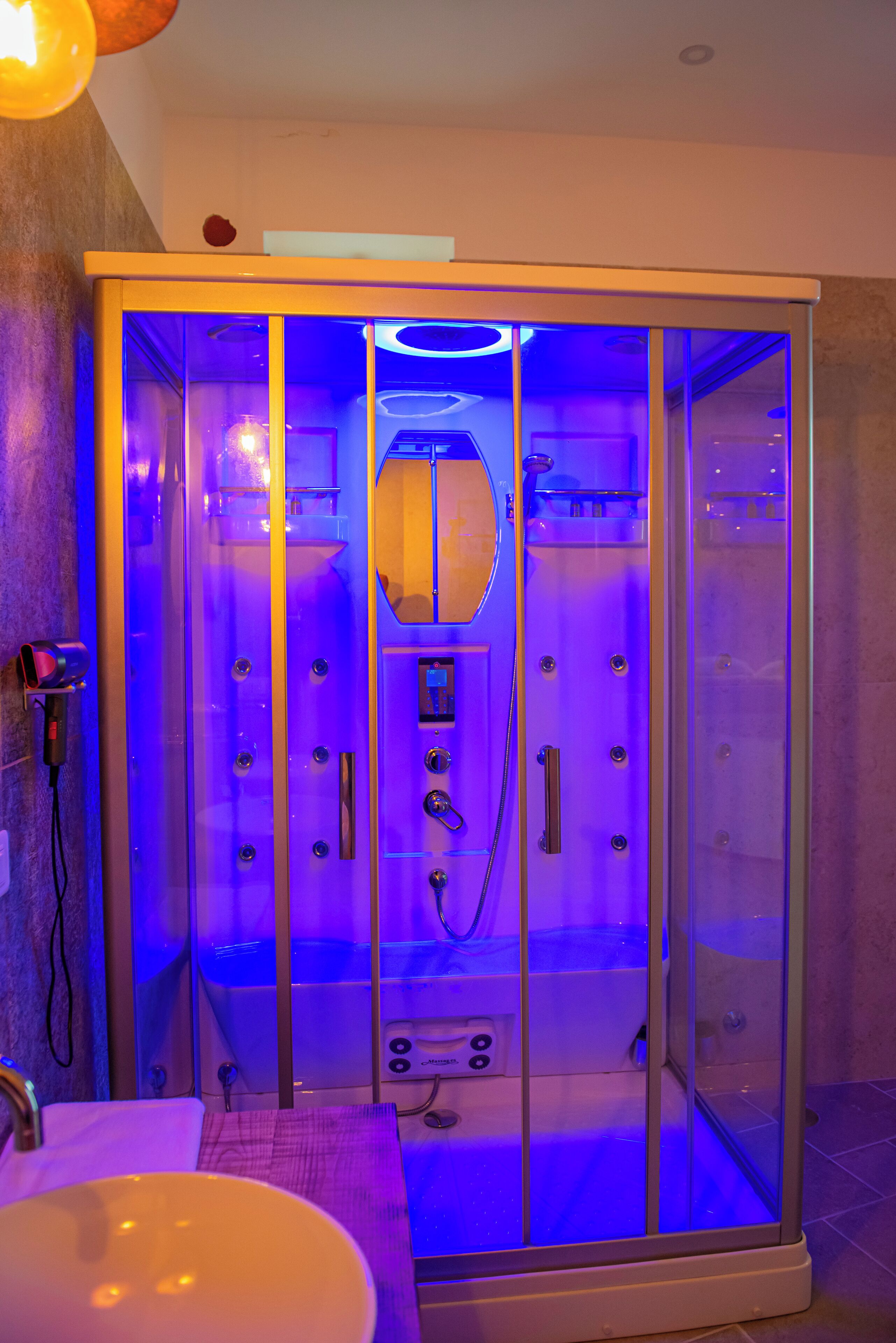A glass-enclosed sauna with a control panel and a towel rack inside.