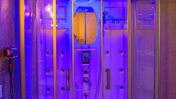 A glass-enclosed sauna with a control panel and a towel rack inside.