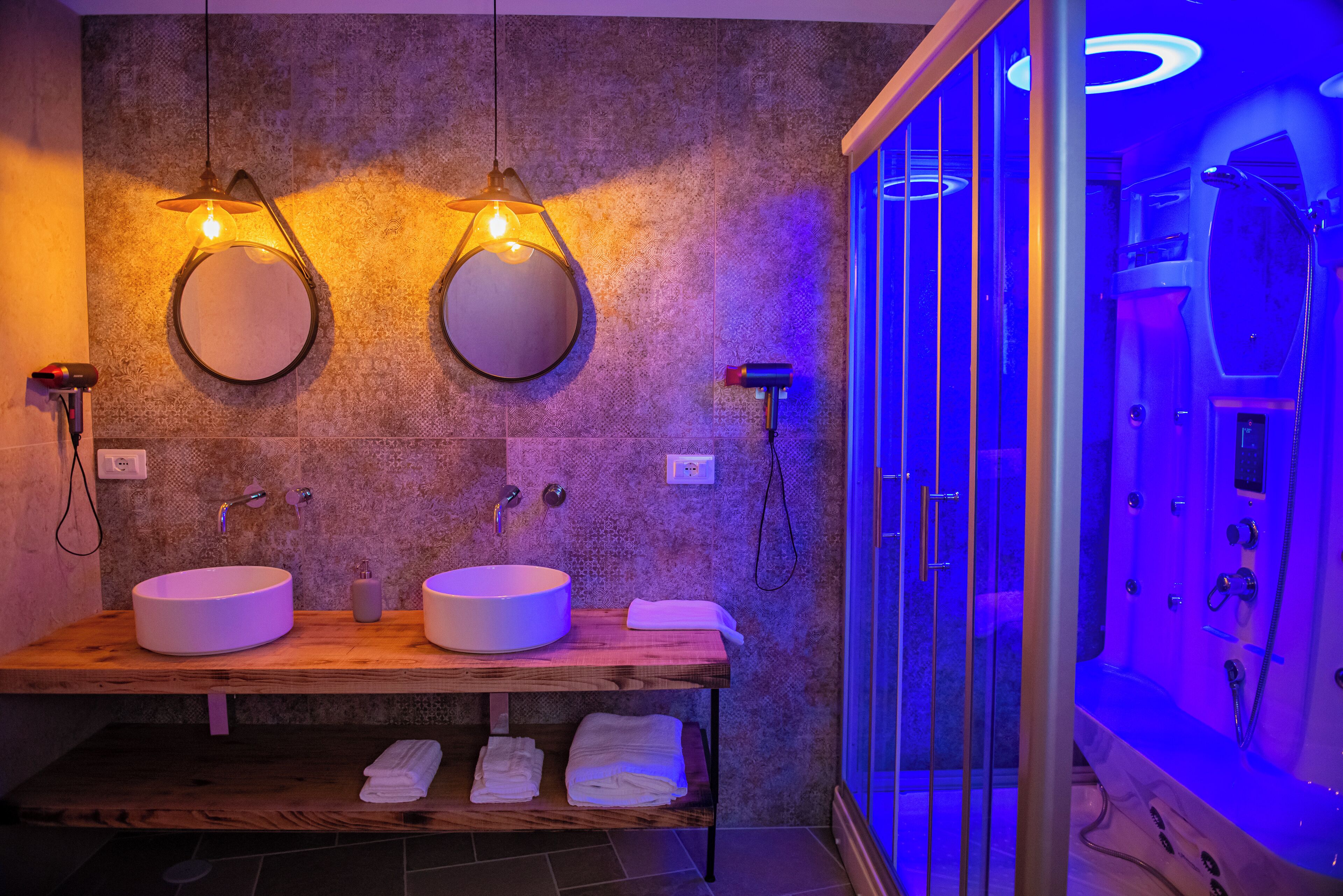 Ein modernes Badezimmer mit zwei Waschbecken, einer Holzausstattung, einer Duschkabine und Wandleuchten.