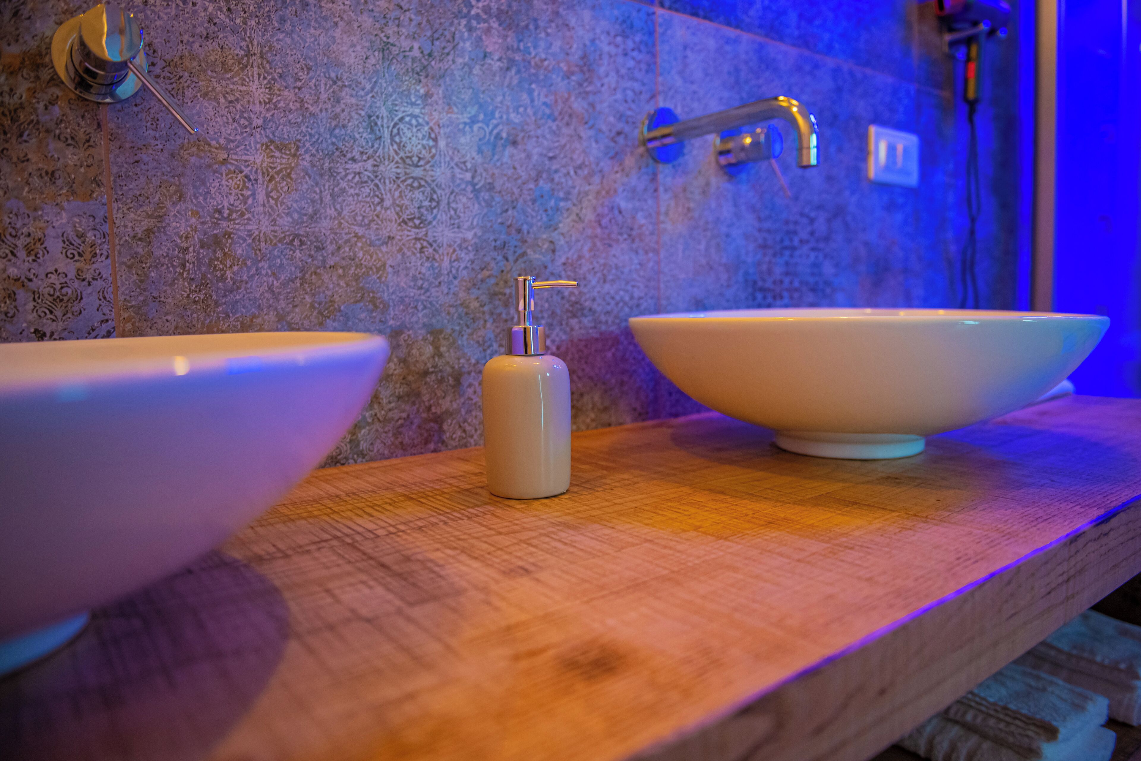 A bathroom with two large white sinks on a wooden countertop, a soap dispenser, and a shower with a handheld showerhead.