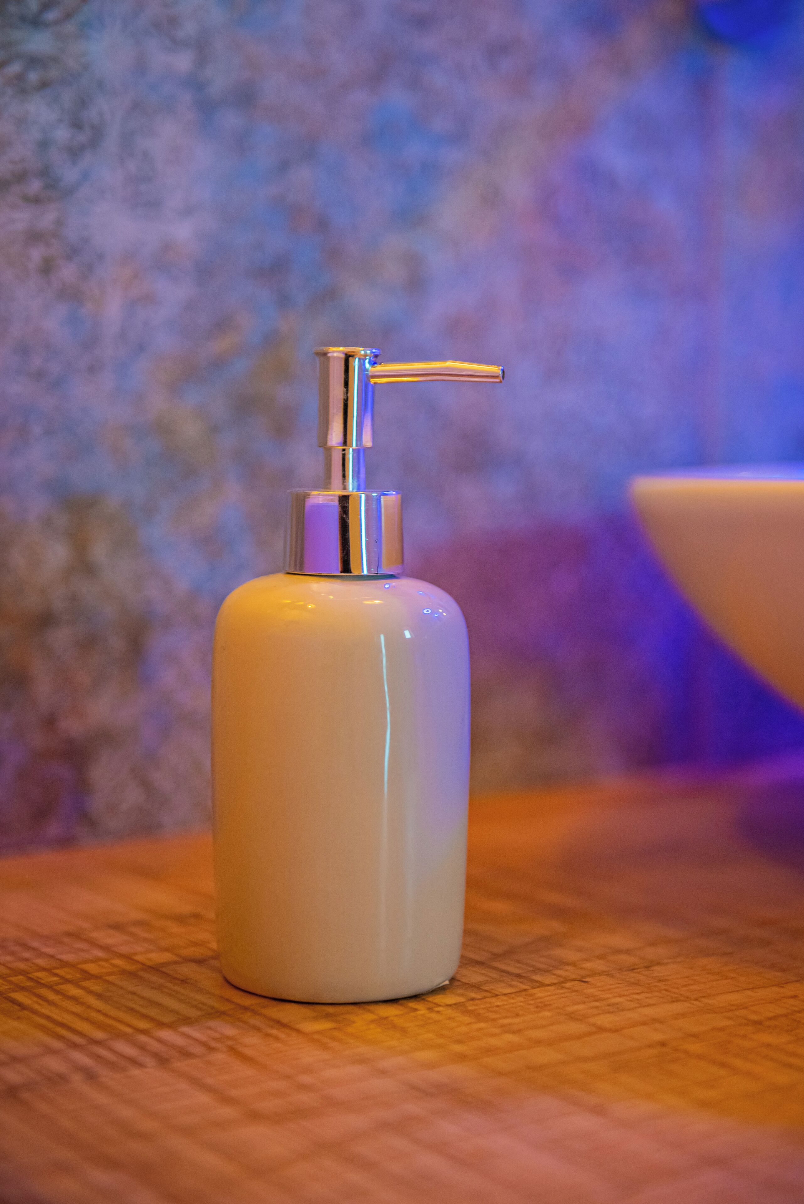 A white pump bottle on a wooden surface with a textured wall in the background.
