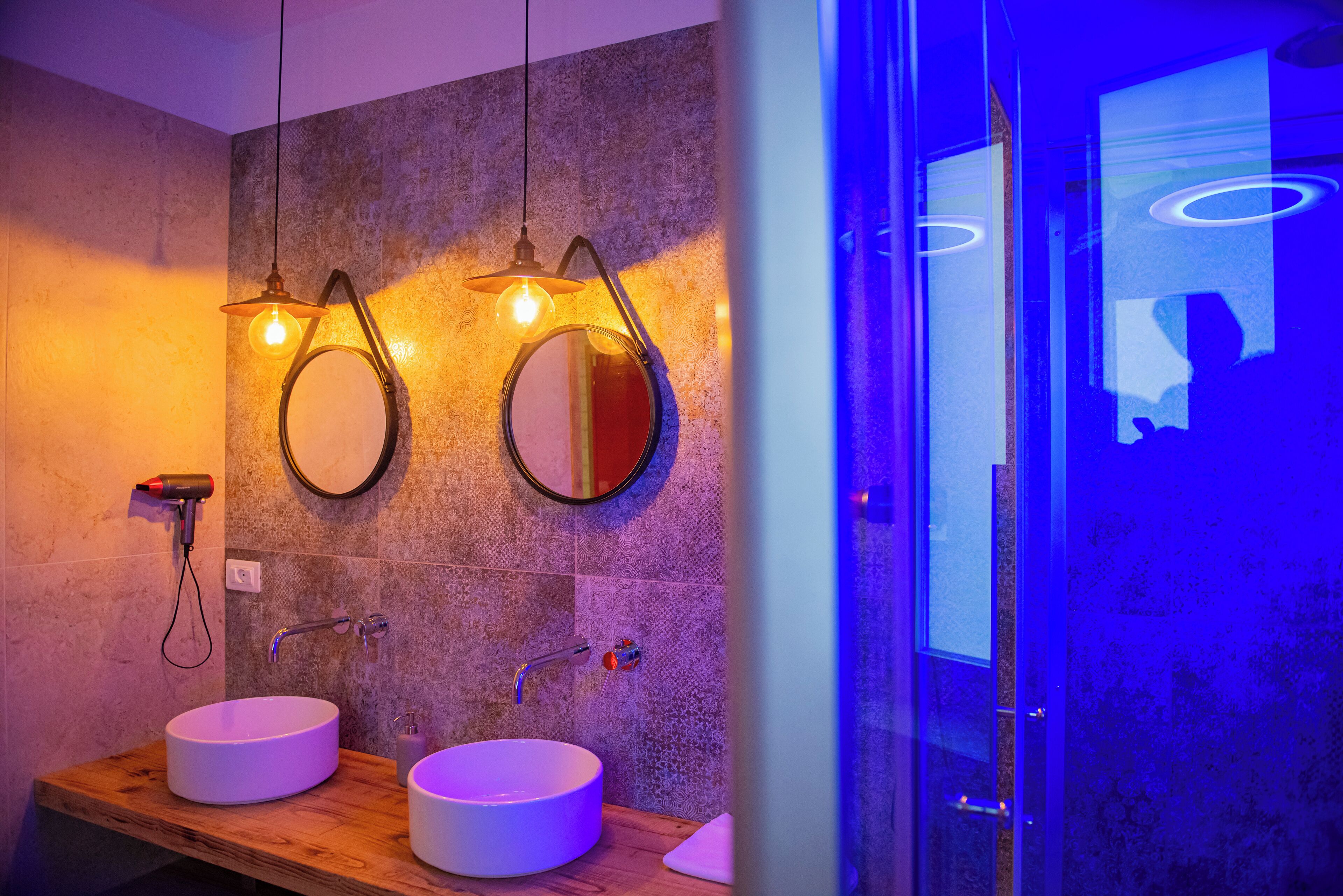 A bathroom with two round mirrors, a wooden vanity, a white sink, and a glass shower enclosure.