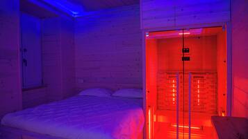 Una habitación con cama, pared de madera y zona de sauna con puerta de vidrio y pantalla digital.