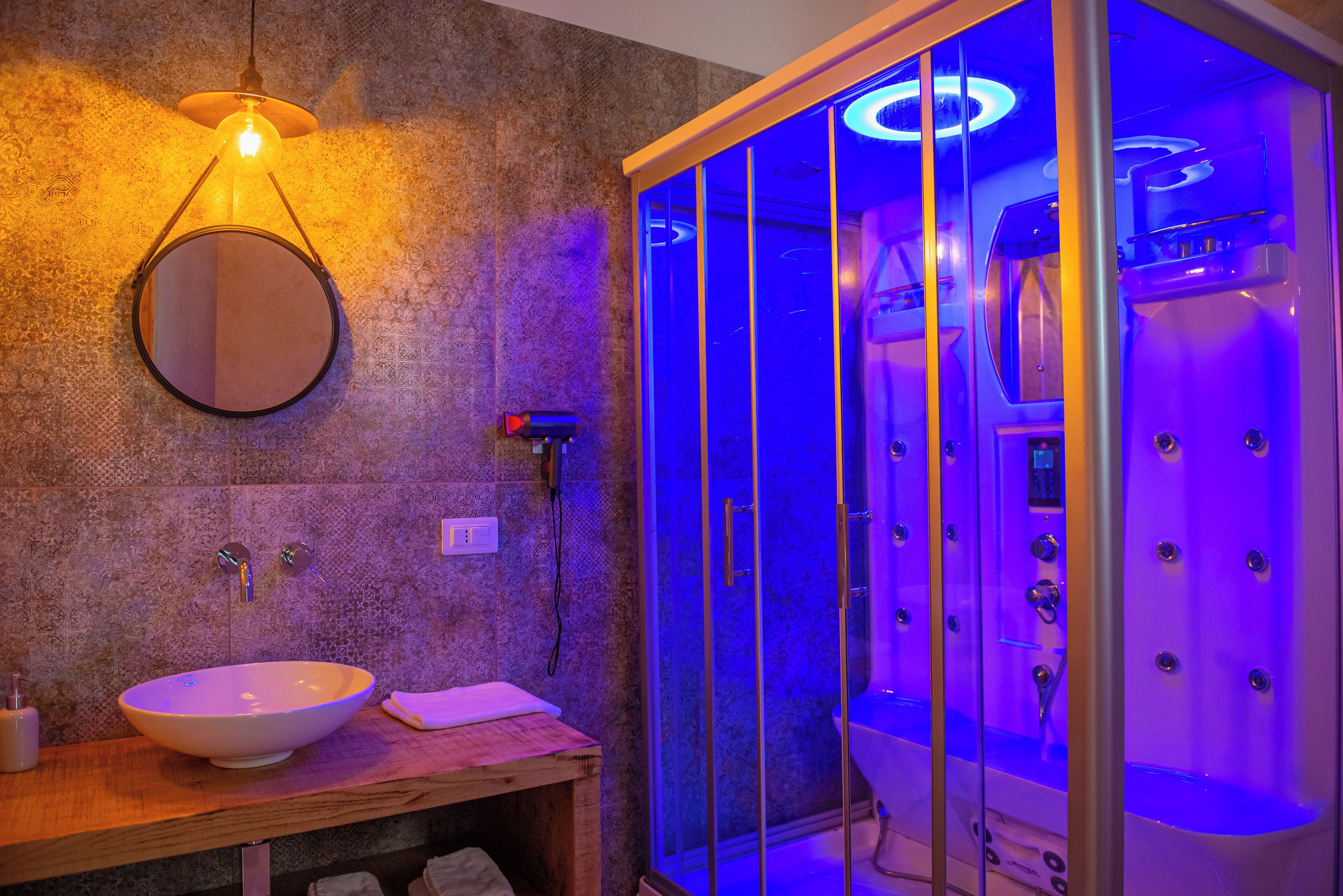 A bathroom with a round sink, a mirror, and a glass-enclosed steam shower with multiple jets.