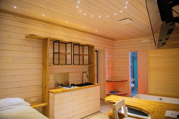 A compact cabin with a kitchenette, a single bed, and a small bathroom.