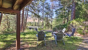 Un área de estar al aire libre con sillas de metal y una mesa, rodeada de árboles y una pérgola de madera.
