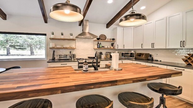 Una cocina moderna con una isla grande, taburetes de madera, armarios blancos e iluminación colgante.