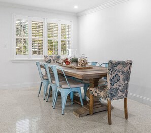 Une salle à manger avec une table en bois, des chaises bleues et une fenêtre avec des volets.