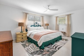 Quarto com cama, mesas de cabeceira, ventilador de teto e janela com cortinas.
