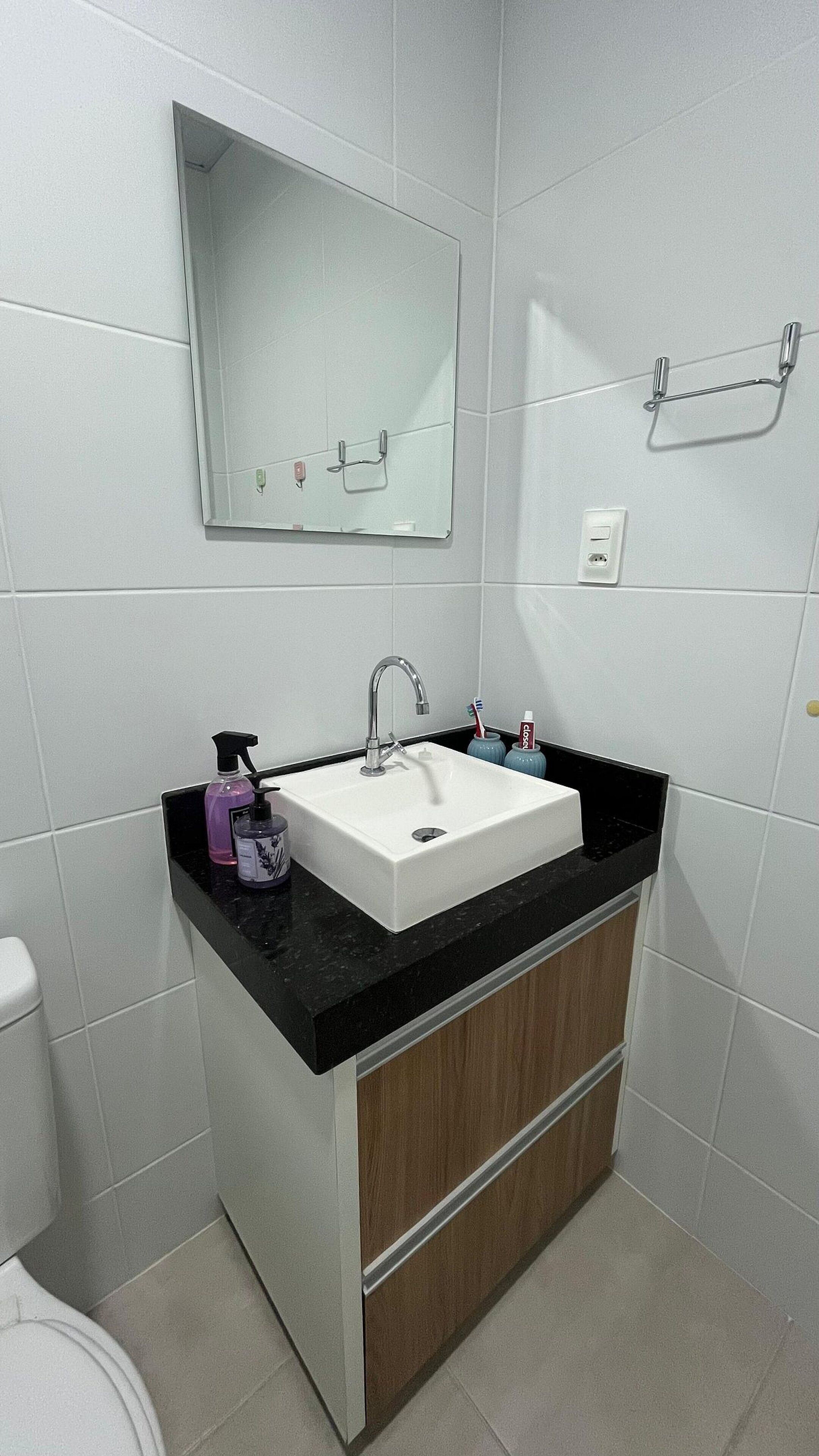 Un baño con lavamanos blanco, encimera negra y armario de madera. Hay un espejo sobre el lavamanos y un perchero en la pared.
