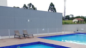 A swimming pool with blue tiles, two lounge chairs, and a grey wall in the background. - Apartamento Refugio das Ondas - Piscina (Palhoça)