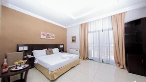 Une chambre d’hôtel comprenant un lit, des tables de chevet, un bureau avec une chaise, une télévision et une grande fenêtre avec des rideaux.