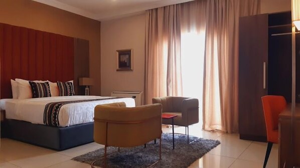 A hotel room with a large bed, a desk, two chairs, and a wardrobe. - Noktel Resort Hotel (Ilorin)