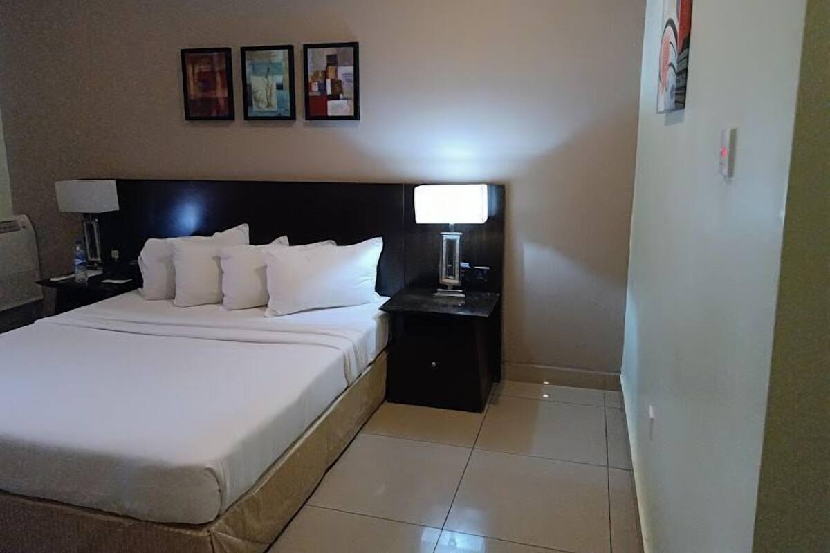 Ein Hotelzimmer mit einem großen Bett, einem Nachttisch mit Lampe und drei gerahmten Bildern an der Wand.