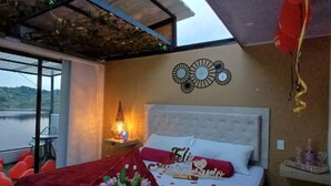 A bedroom with a bed, a nightstand, a wall-mounted light, and a view of a body of water. - Hotel y Termales Castillo del Lago (El Peñol)