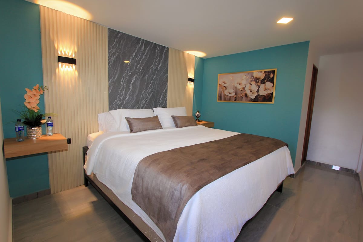 A modern hotel room with a large bed, a nightstand, a vase with flowers, and a painting on the wall.