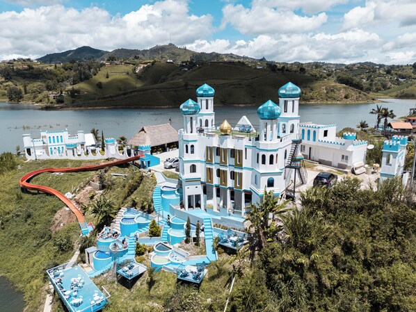 Un edificio grande y blanco con detalles azules y varias torres, rodeado de agua y vegetación.