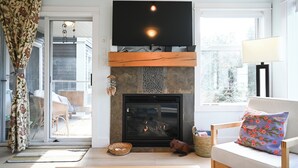 A living room with a fireplace, a flat-screen TV, a sofa with a cushion, and a window with a view.