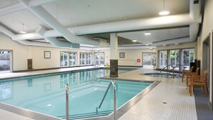 An indoor swimming pool with clear water, tiled floor, and safety railings.