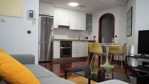 A modern kitchen with white cabinets, a stainless steel refrigerator, and a microwave. There is a dining area with yellow chairs and a small table. - Centrally located apartment in Vigo 5 minutes from Puerta del Sol (Vigo)