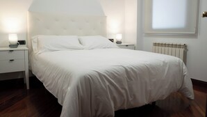 A neatly made bed with white linens, two bedside tables with lamps, a radiator, and a window with blinds. - Centrally located apartment in Vigo 5 minutes from Puerta del Sol (Vigo)