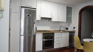 A kitchen with stainless steel appliances, white cabinets, a microwave, and a yellow chair. - Centrally located apartment in Vigo 5 minutes from Puerta del Sol (Vigo)