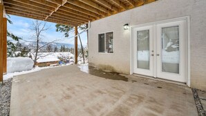 A covered outdoor area with a concrete floor, wooden beams, and a white exterior wall with a sliding glass door.