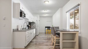 A modern kitchen with white cabinets, a microwave, and a coffee maker. There is a dining area with a table and chairs.