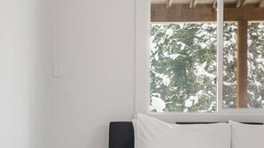A bedroom with a bed, a nightstand, a window, and a view of trees.