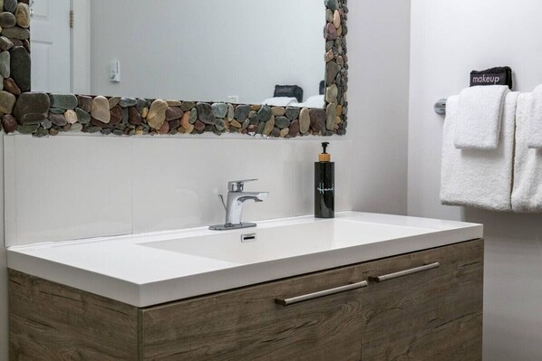 A bathroom with a white sink, a mirror with a stone border, a wooden cabinet below the sink, and a towel rack with a white towel.