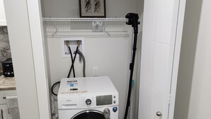 Ein kleiner Waschraum mit einer Frontlader-Waschmaschine und einem Trockner, einer Schlauchaufrolle und einem Schild mit der Aufschrift 'Waschen Trocknen'.
