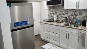 Eine moderne Küche mit weißen Schränken, einem Edelstahl-Kühlschrank, einer Mikrowelle und einer Marmor-Spritzschutzwand.