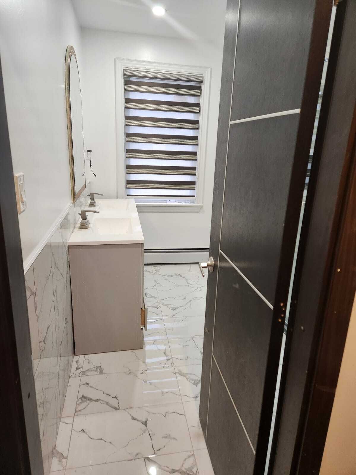 Un baño con tocador blanco, espejo y ventana con persianas horizontales.