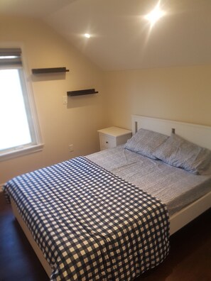 A bedroom with a bed, a nightstand, a window, and a wall-mounted shelf. - Room in Guest Room - Queen Room 2 Brampton Toronto Canada (Brampton)