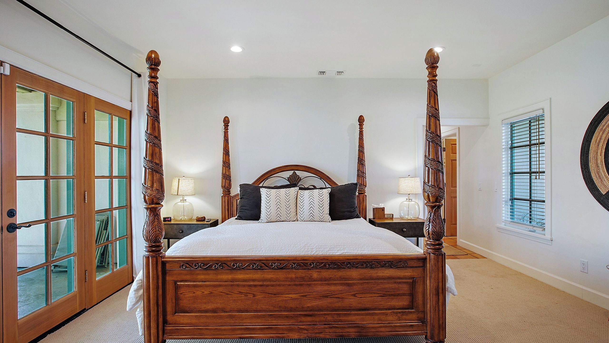 Un lit à baldaquin avec une tête de lit en bois, deux tables de chevet avec des lampes et un grand miroir au mur.