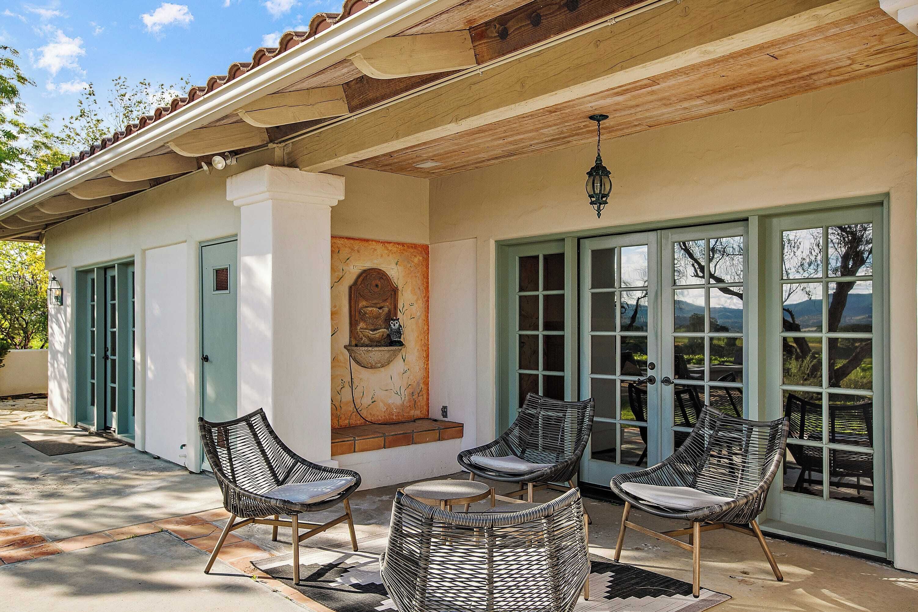 A covered patio with wicker chairs and a table, a mural on the wall, and a view through large glass doors.