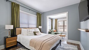A bedroom with a bed, bedside tables, a TV, and a view of the outside.